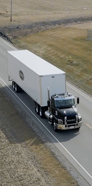 A Mack semitruck with Strick trailer drives down a rural highway A Mack semitruck with Strick trailer drives down a rural highway