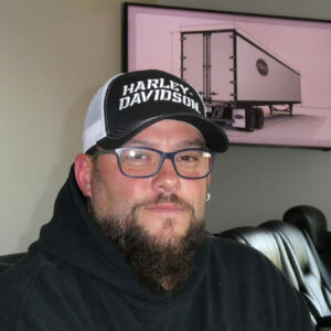 Man with glasses, beard and hat wearing black hooded sweatshirt